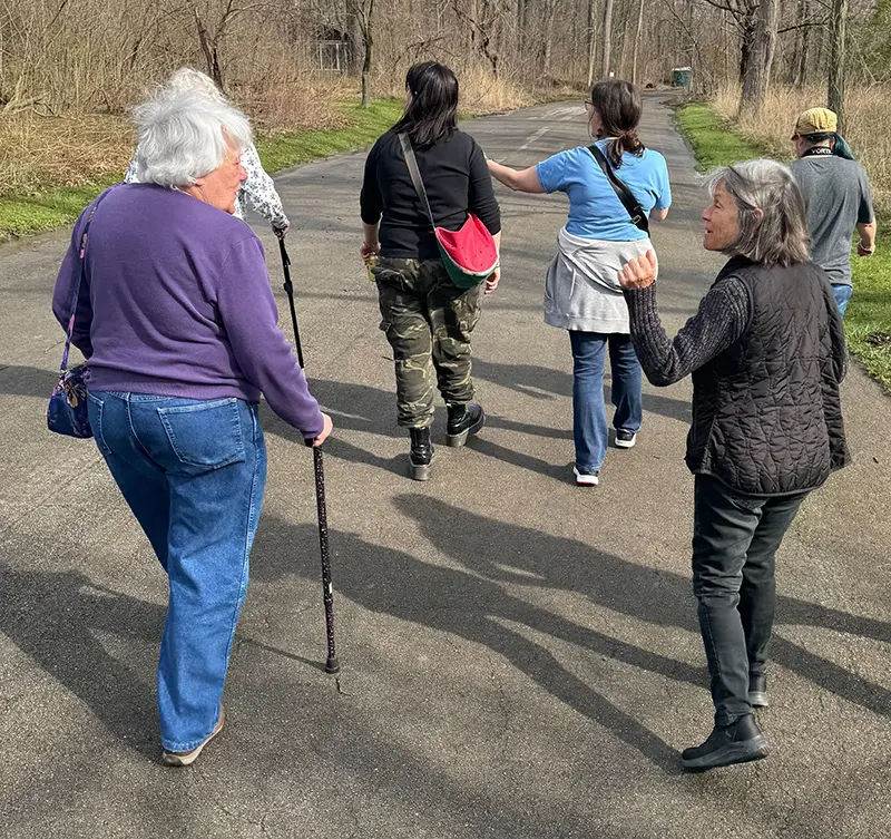 a group of women walking near trees, one with a cane