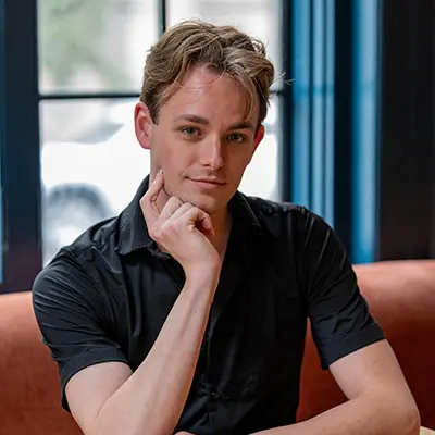 Drew seated at a wooden table, chin resting on his hand, wearing a black shirt