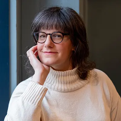 Jackie Ross wearing a cream turtleneck and black-rimmed glasses