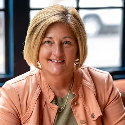 Julie Womack sitting in front of a window wearing a sage shirt and salmon jacket