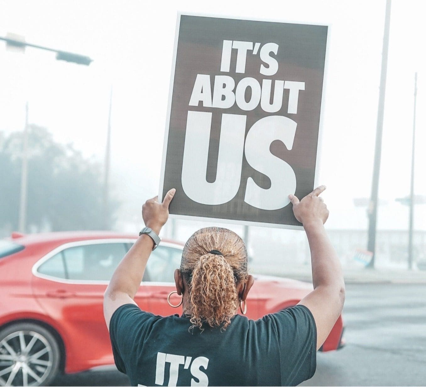 woman holding sign saying 'It's about us'